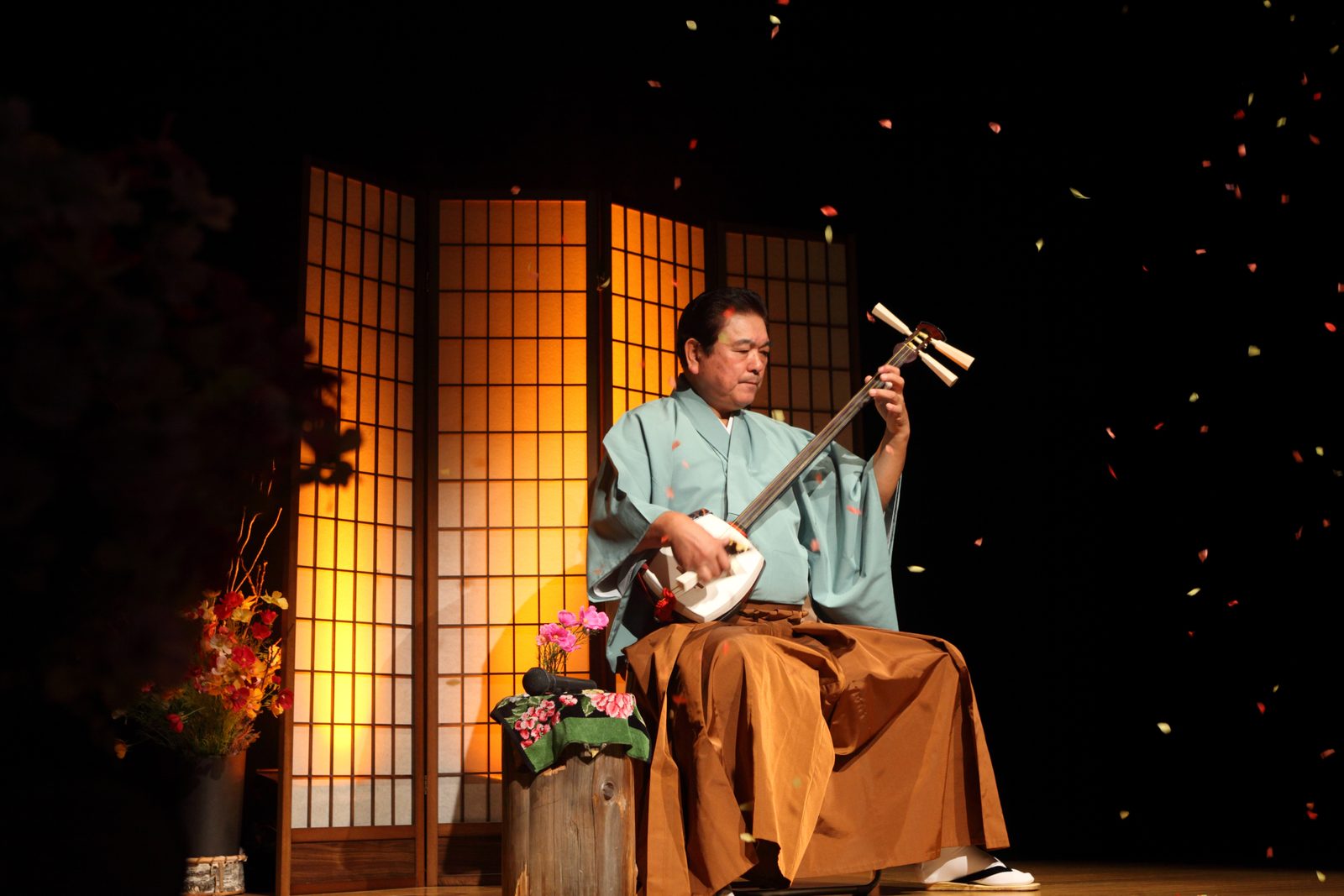 A performer in a green kimono playing the shamisen on stage at the Tsugaru Shamisen Hall