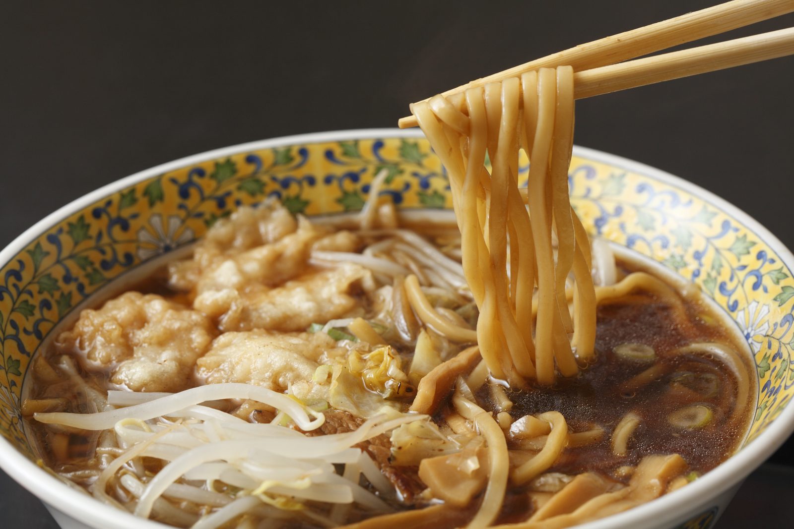 A bowl of Kuroishi tsuyu yakisoba, thick noodles in a dark soy broth topped with bean sprouts and tempura crumbs, with a portion lifted on chopsticks