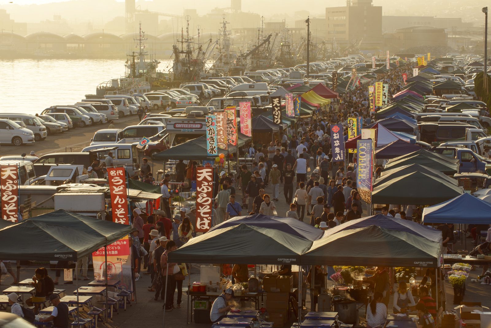 Rows of tents and stalls along the quay at the Tategahana Sunday morning market, with fishing boats moored behind