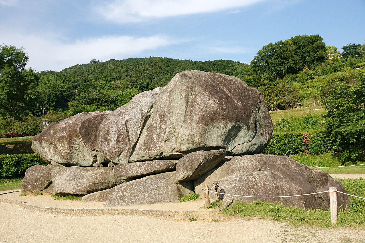 The exposed granite chamber of the Ishibutai burial mound in Asuka, a huge capstone resting on lower boulders in front of a wooded hillside.