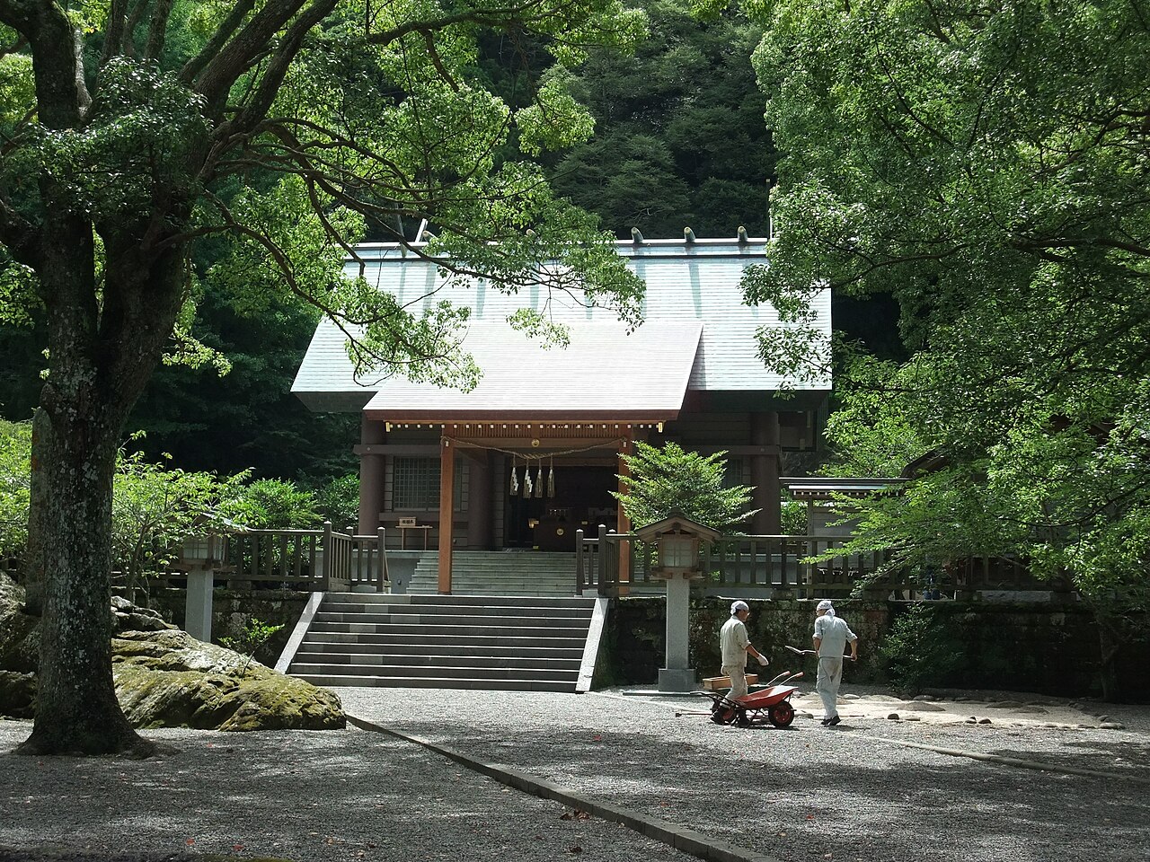 Worshippers' approach to Awa Jinja's hall of worship beneath tall trees and a stone stairway