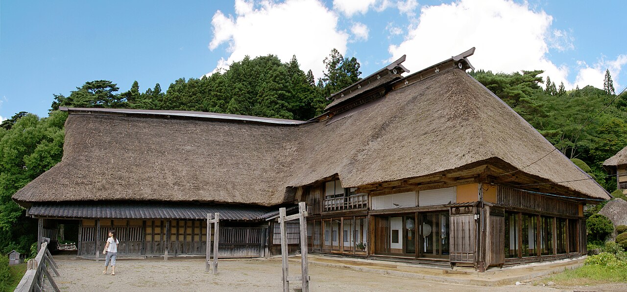 The Chiba family's L-shaped Nanbu magariya farmhouse in Tono, its long thatched roof sweeping down over the stable wing and the main house.