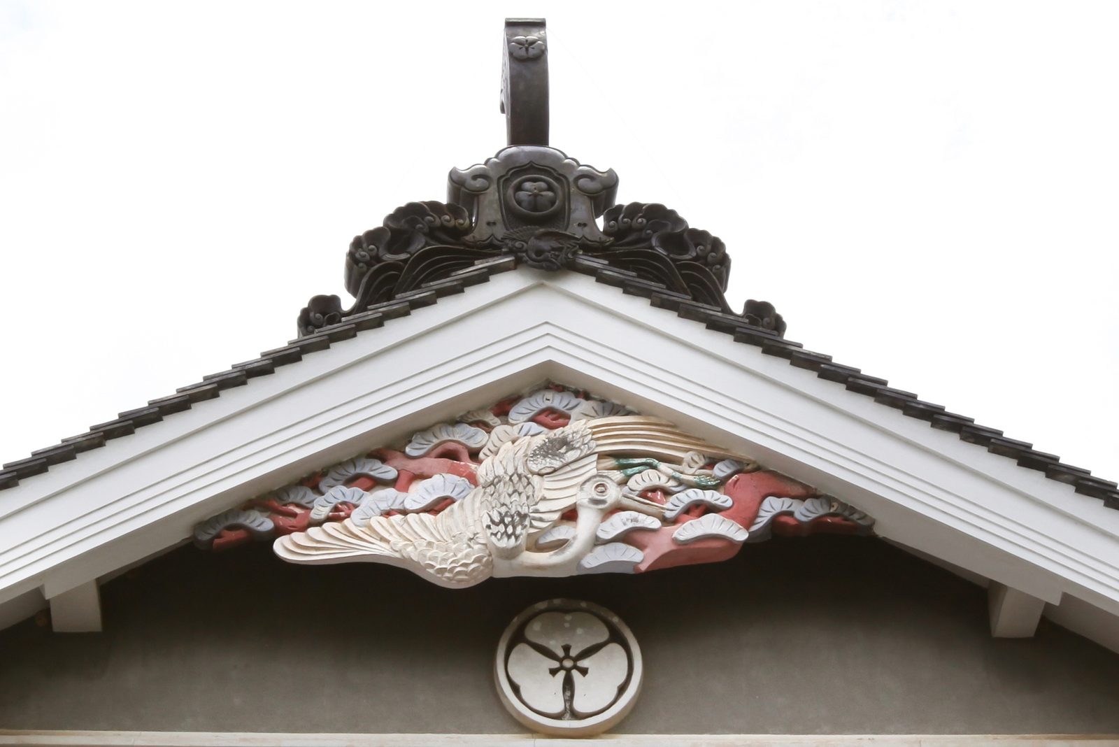 Close-up of a gable with a carved crane among pine branches, a family crest below and an ornate ridge-end tile above