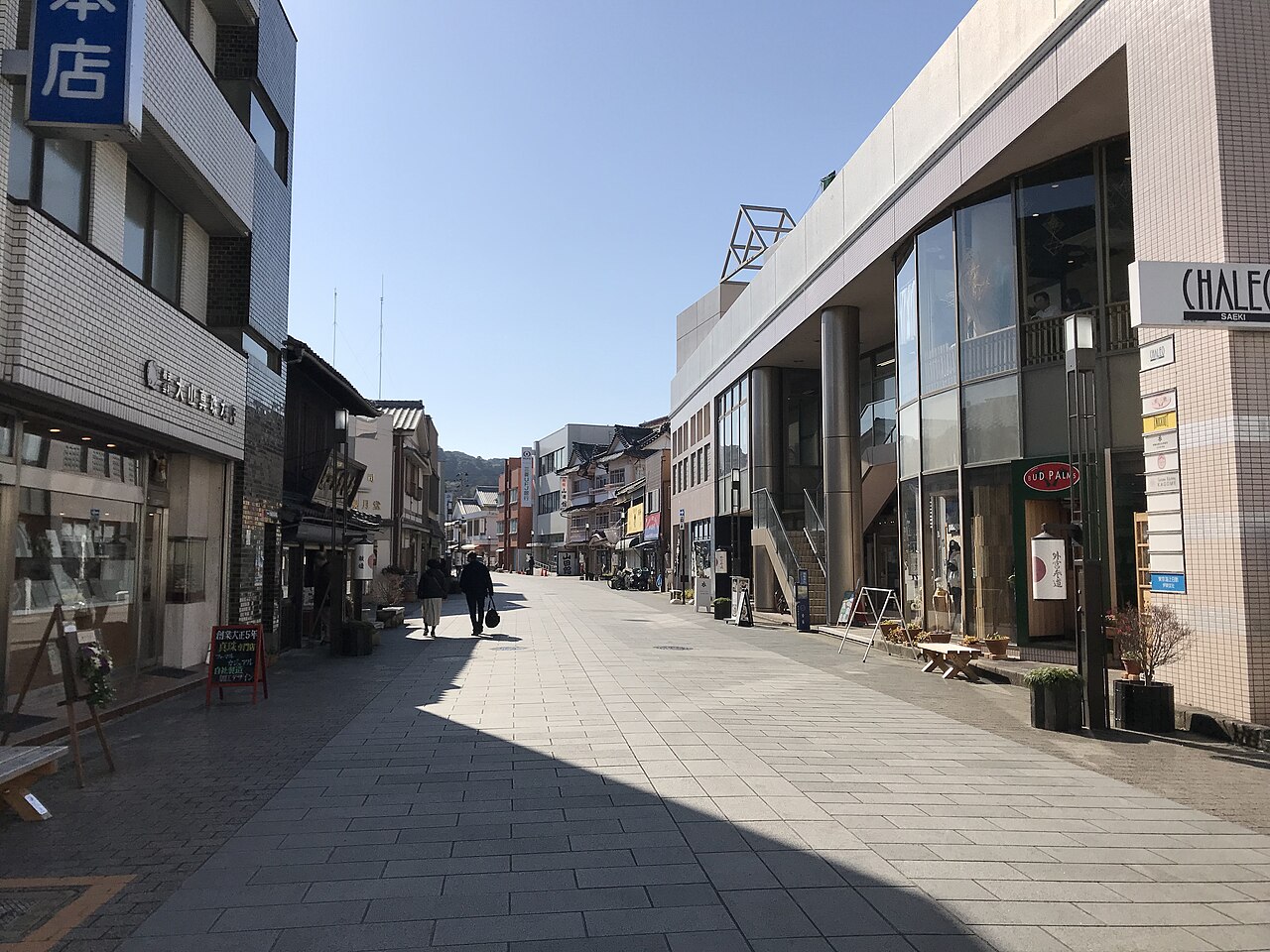 A tidy shopping street on the Outer Shrine approach, with a pedestrian walking past low wooden storefronts