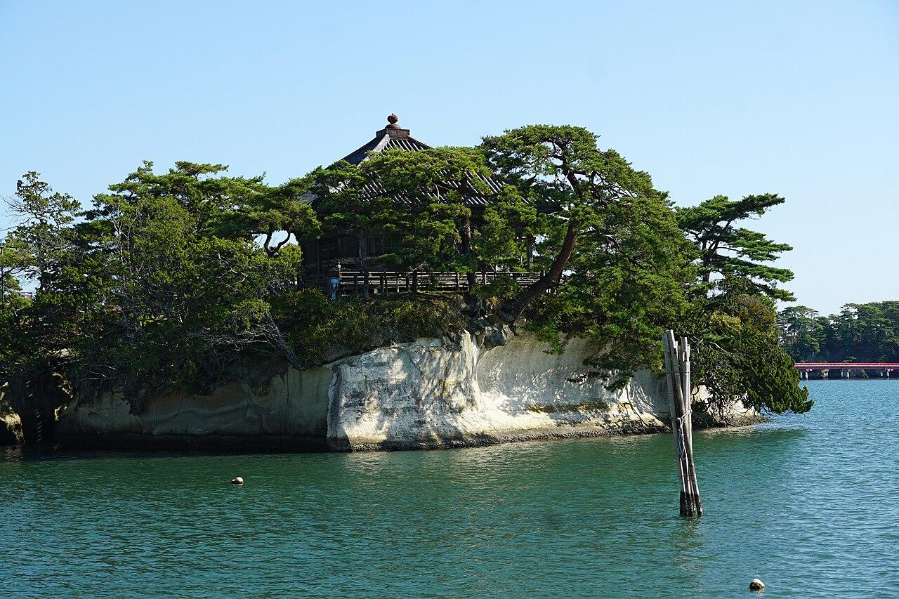 Godaido hall standing among pines on its small rocky islet, with the pale rock face rising out of the green water of Matsushima Bay