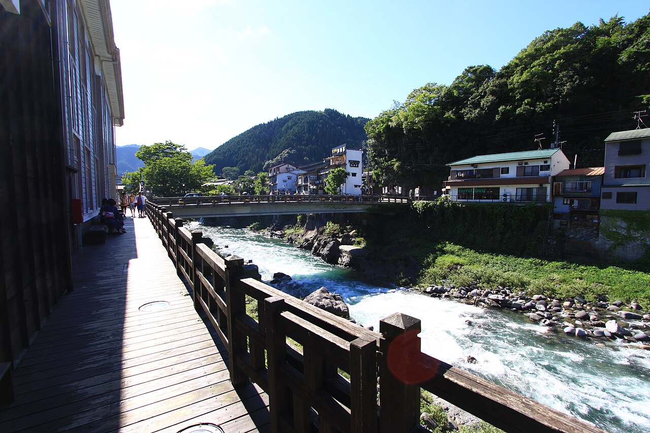 A wooden riverside walkway along the Yoshida River in Gujō Hachiman, with the town's houses and forested hills beyond