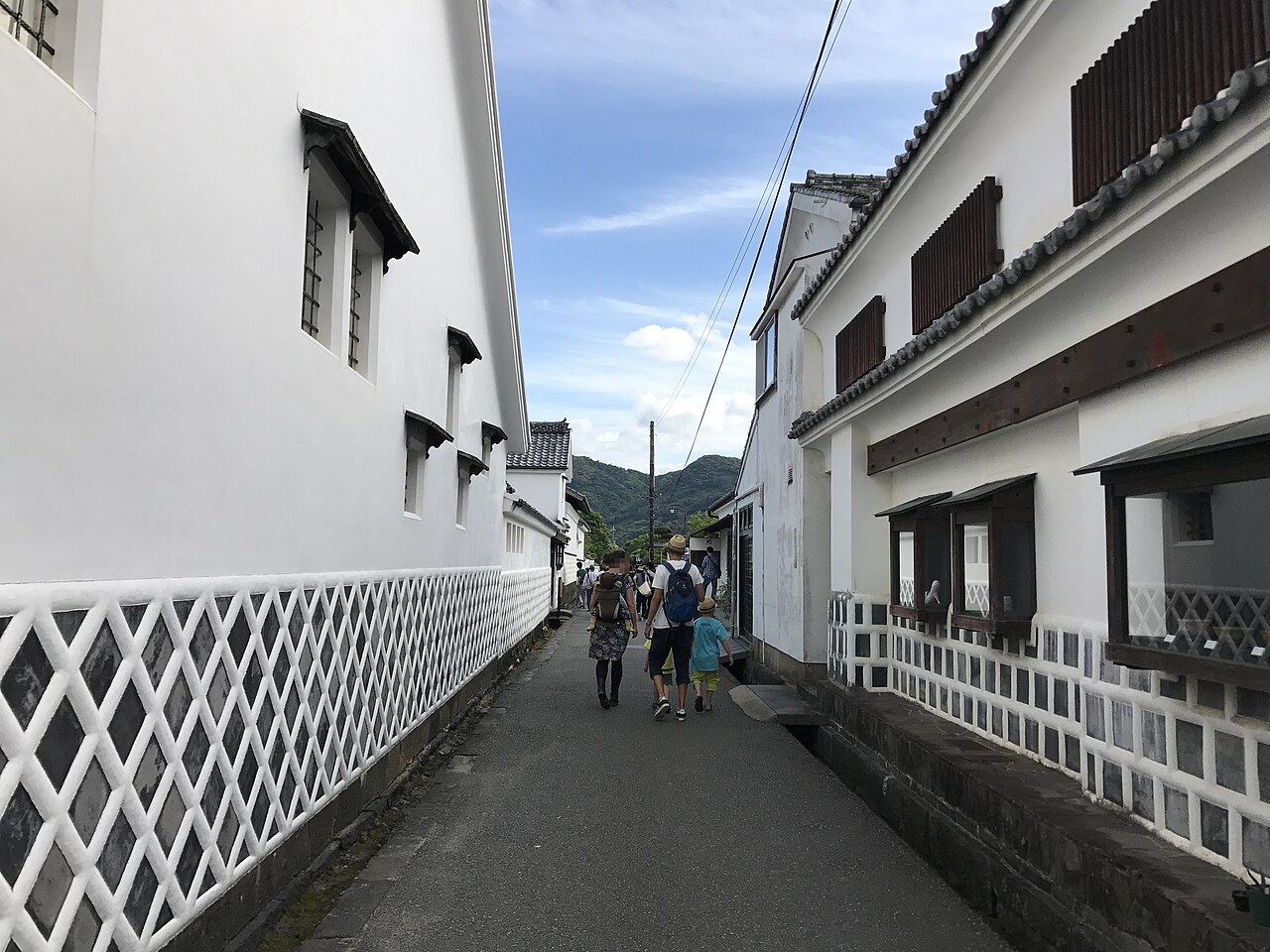 A lane in the Hagi castle town between white plastered walls and diamond-patterned namako tiling, with a family walking away from the camera