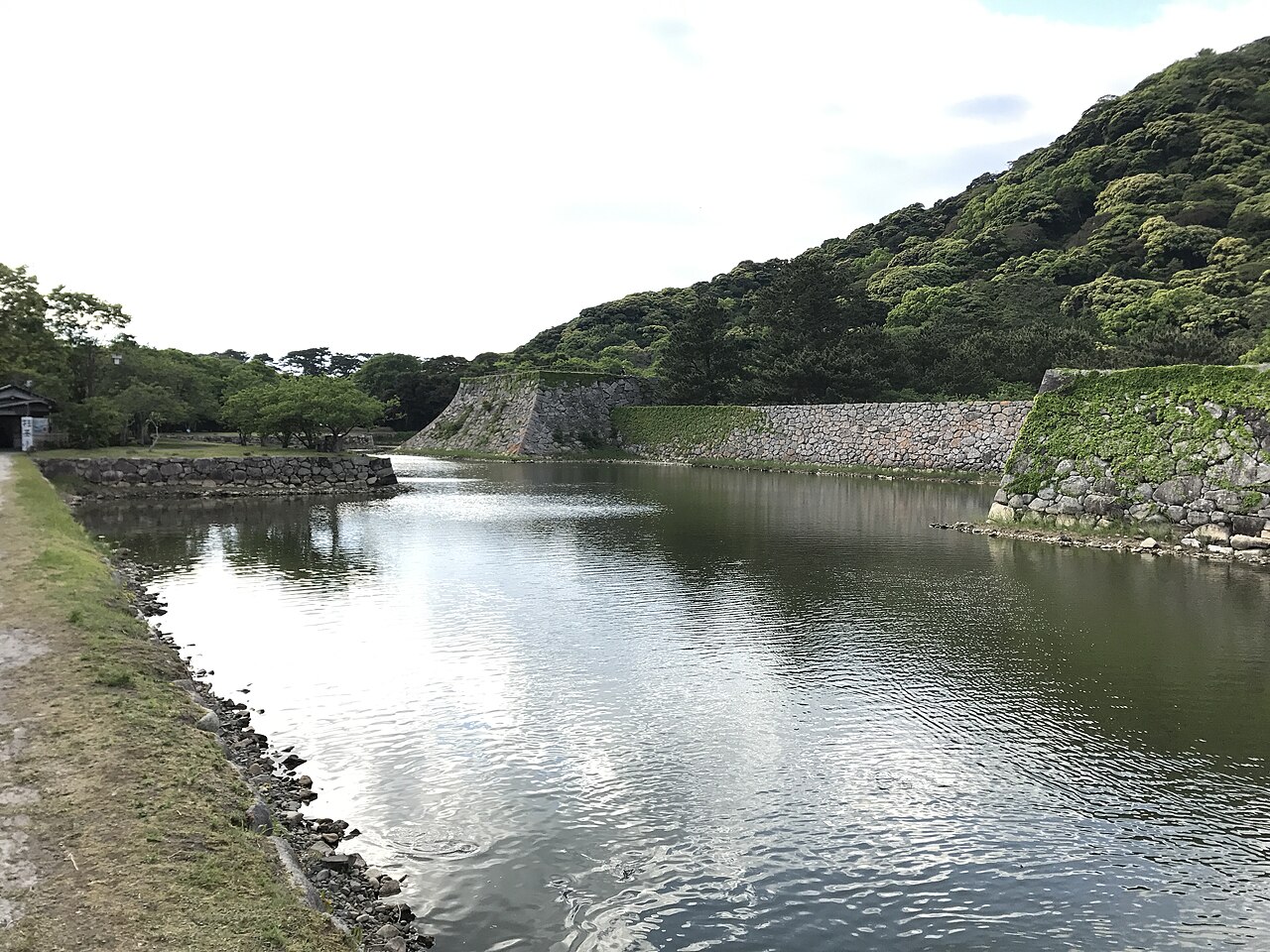 The water-filled moat and the dry-laid stone base of the vanished keep at Hagi Castle, with wooded Mount Shizuki behind