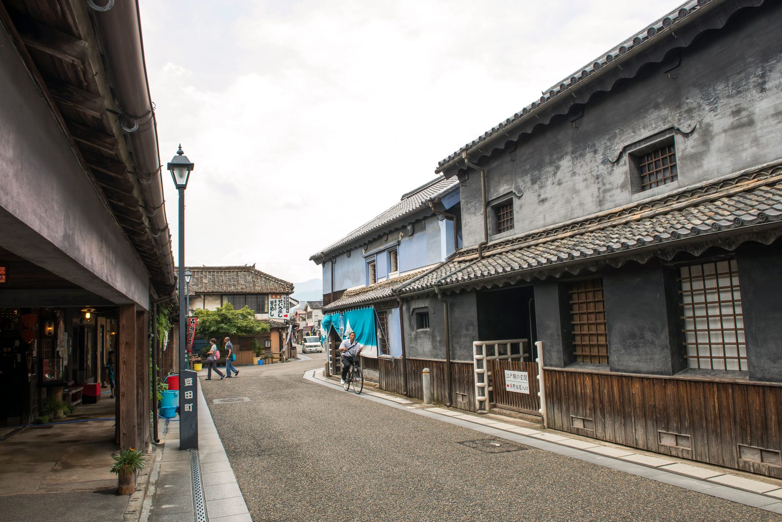 A quiet side street beside dark plastered storehouse-style buildings with tiled eaves in Mameda-machi, Hita