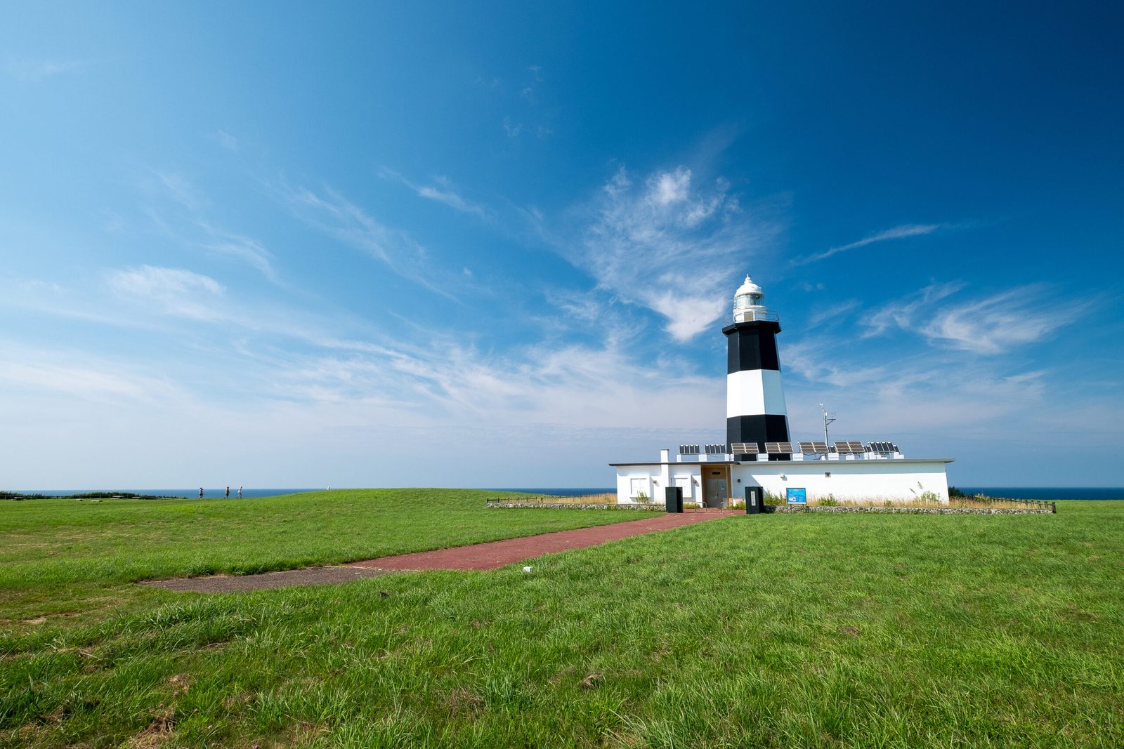 White and black striped lighthouse on a grassy headland