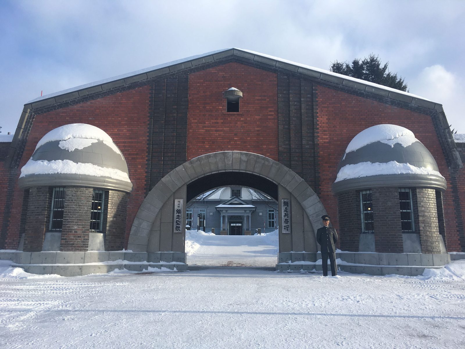 Snow-covered red-brick gate of the prison museum, with a person standing beyond the arch