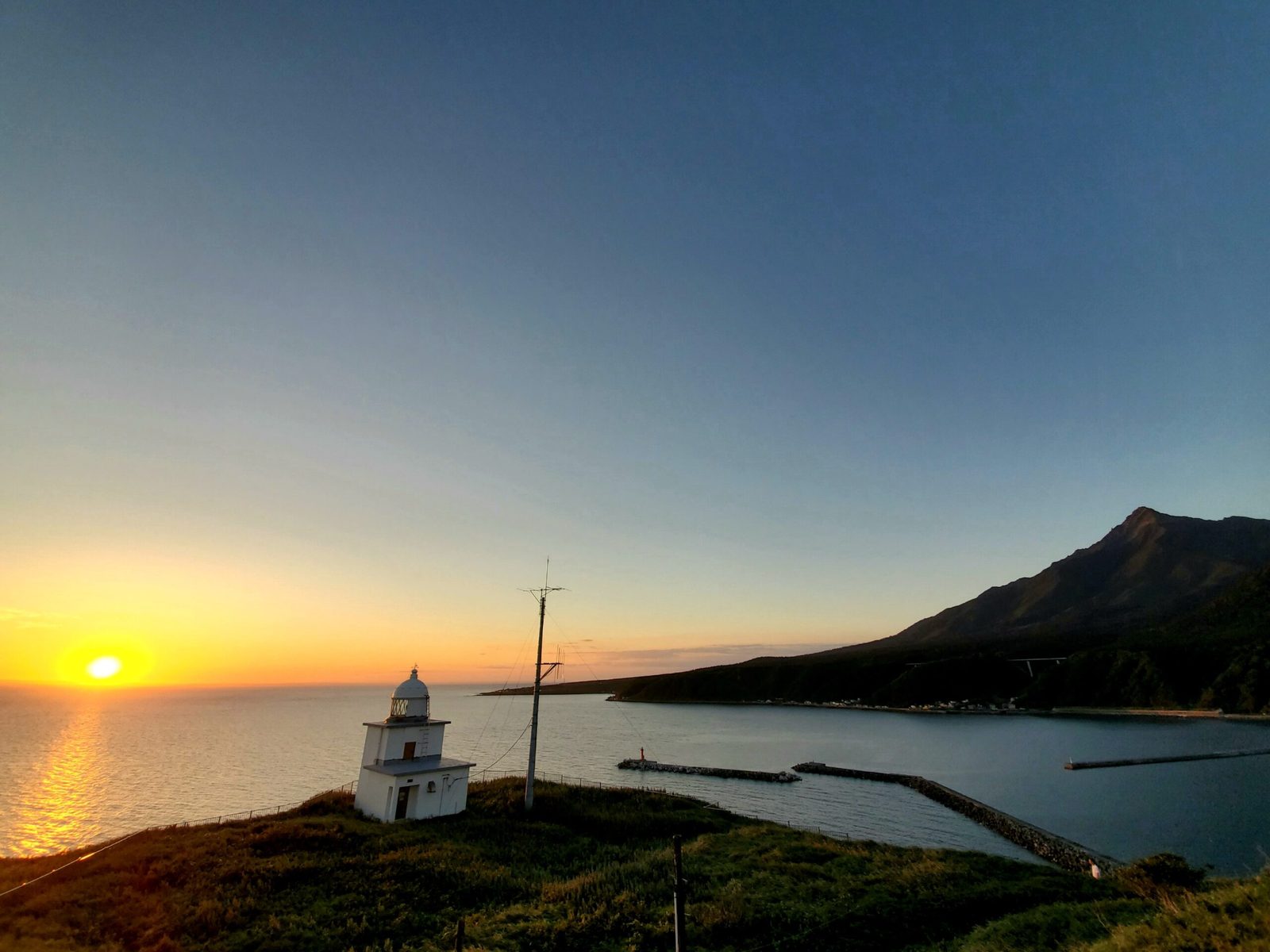 Small white lighthouse on Pesi Cape at sunset, with Mount Rishiri in the background