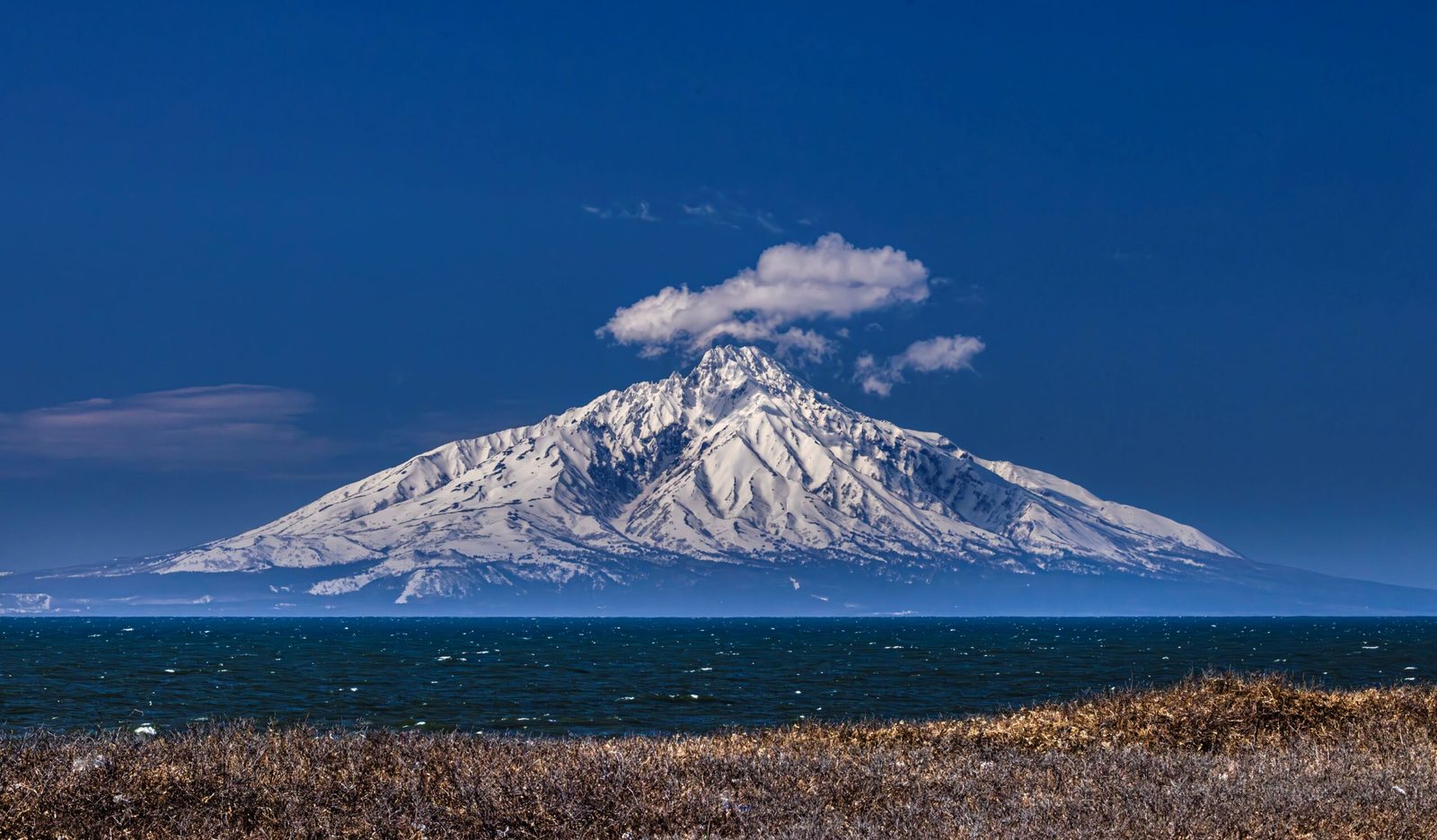 Snow-capped Mount Rishiri rising above the sea under a blue sky with a small cloud over the summit