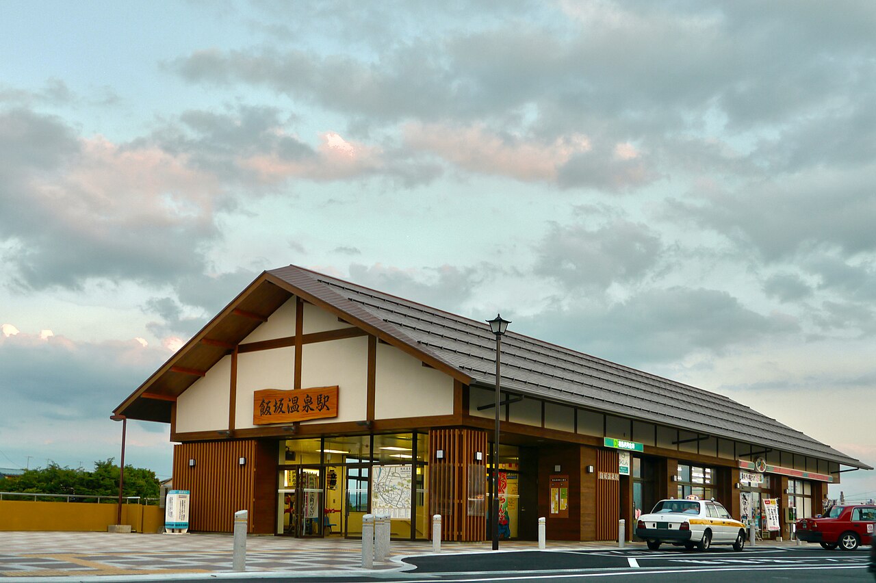 The wooden station building of Iizaka-Onsen at dusk, with a taxi waiting under its wide tiled roof
