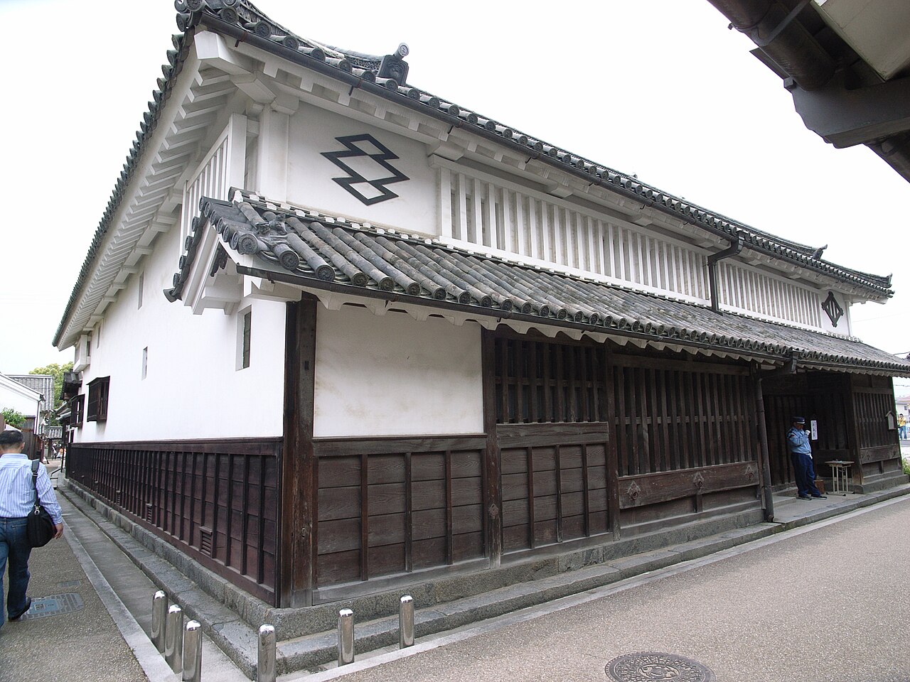 The Imanishi House in Imai-cho, a large wooden merchant residence with a stepped tiled roof, white plaster gable end, and dark timber lattice windows facing the street.