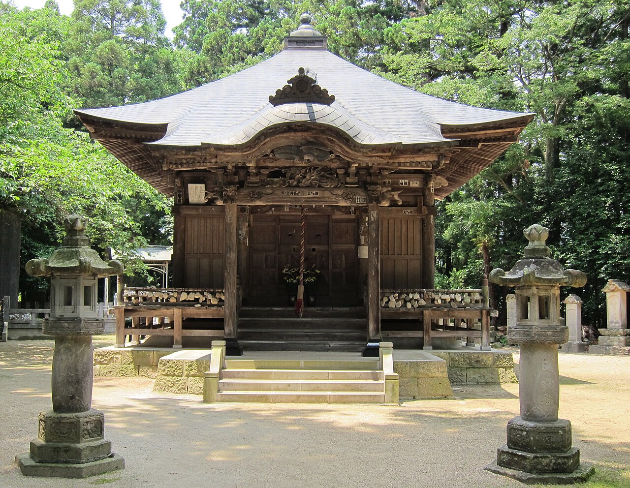 The wooden Yakushi hall of Io-ji standing among tall cedars, with a pair of stone lanterns on the approach