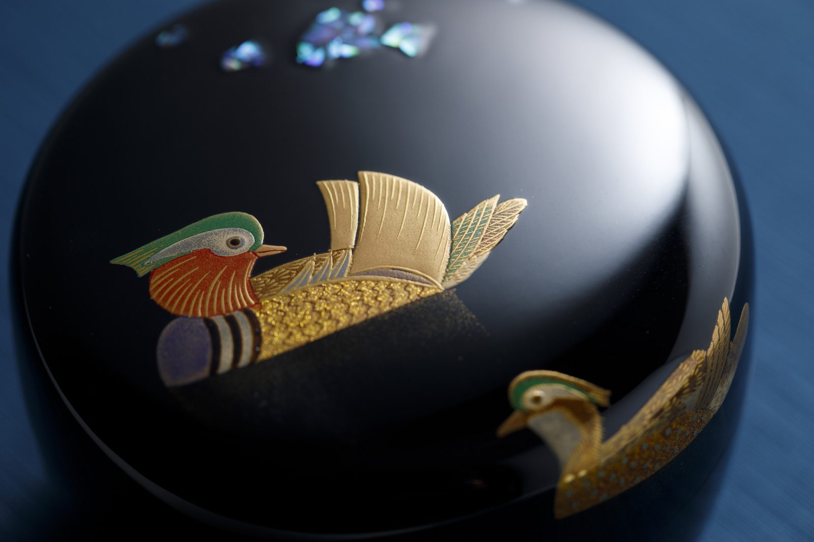 A black lacquer lidded box decorated with gold maki-e mandarin ducks and inlaid shell on a blue background.