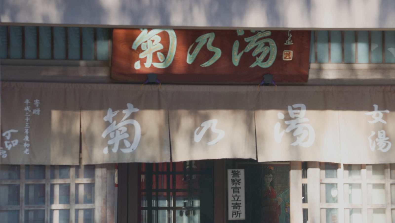 The wooden facade of a public bathhouse with a carved signboard and white curtains at the entrance.