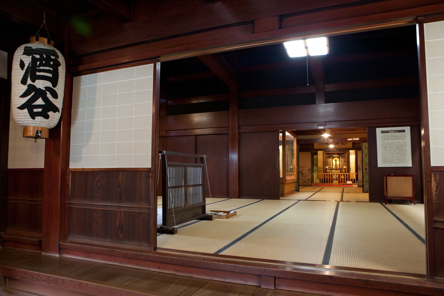 Tatami rooms opening off the earthen-floored entrance of the old shipowner house, with a paper lantern by the door
