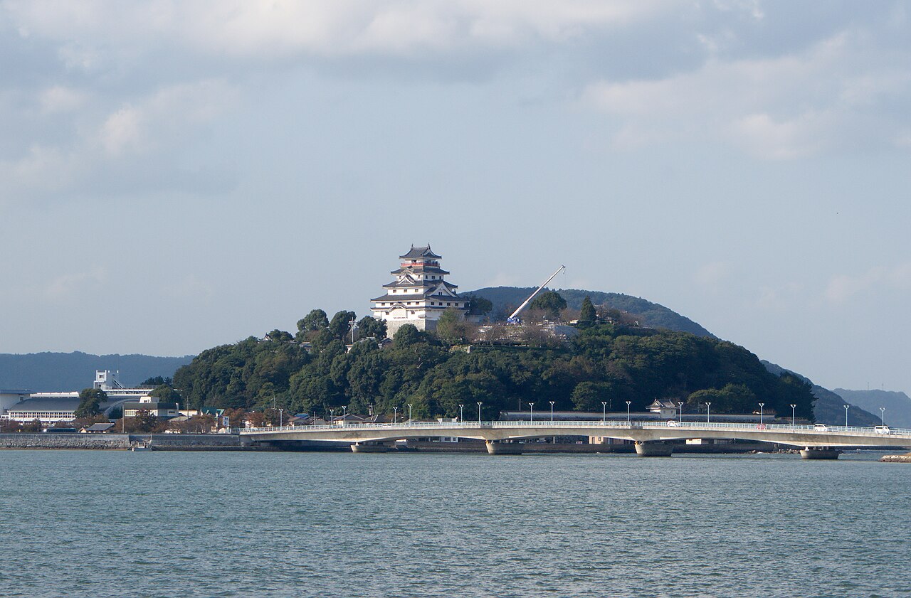 Karatsu Castle's white keep above the trees on its hill across the bay, with Maizuru Bridge crossing the water in the foreground