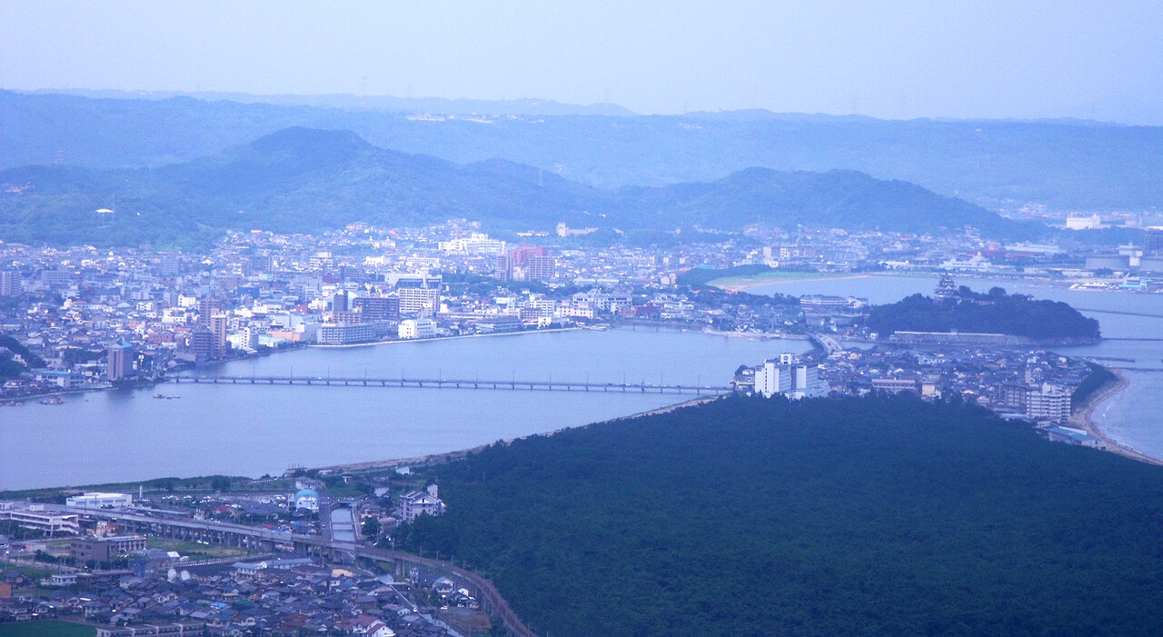 Central Karatsu from above, with the Matsuura River and its long bridge, the town spreading toward the harbor, the castle on its hill and the pine grove along the shore