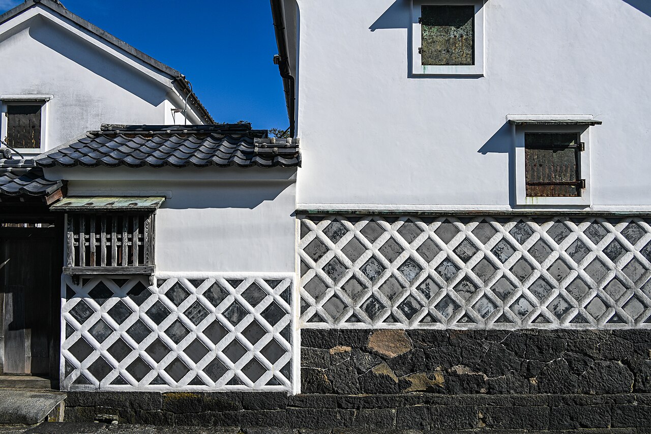 The street wall of the Kikuya merchant house in Hagi: white plaster above diamond-patterned namako tiling on a dark stone base, under deep blue sky