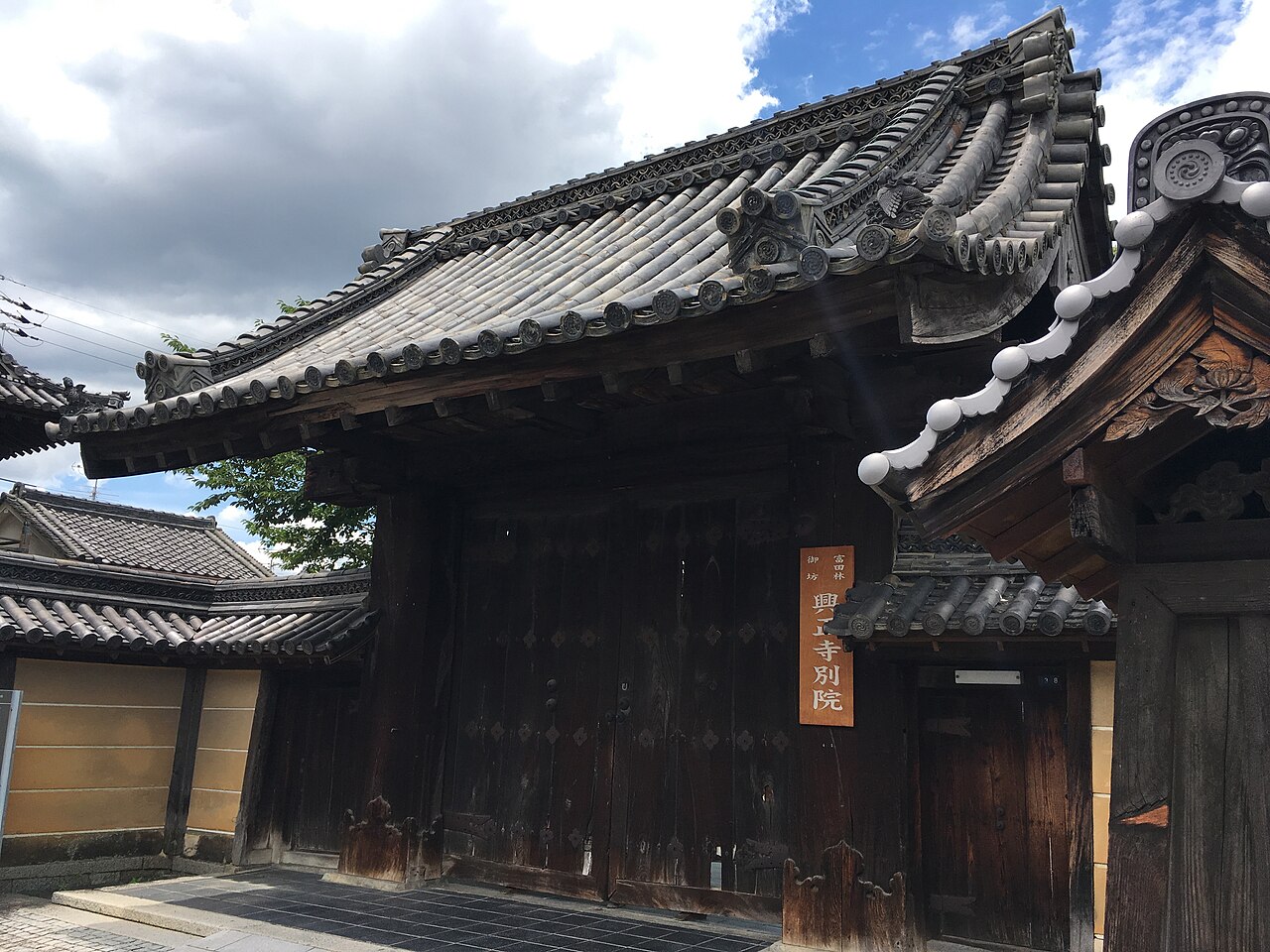The gate of Koshoji Betsuin temple in Tondabayashi, a weathered wooden gate with a heavy tiled roof and a vertical name board