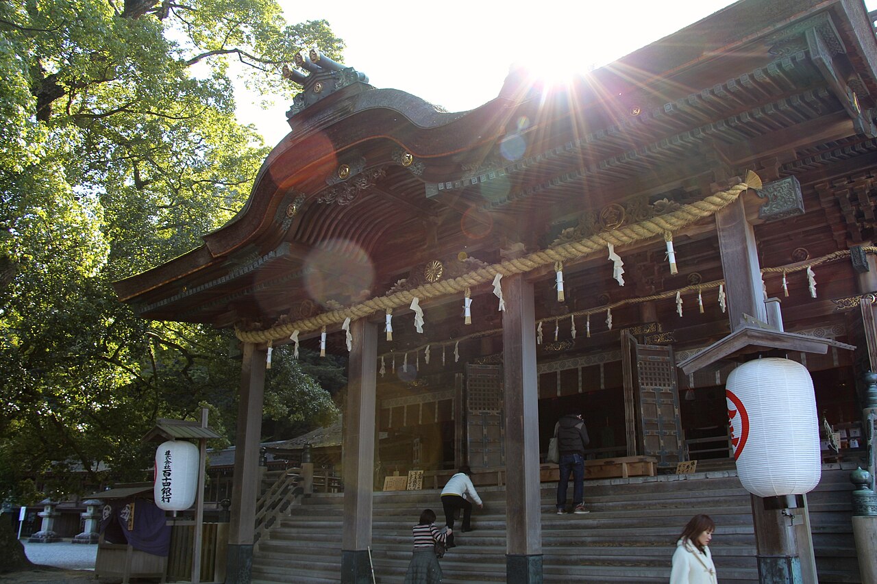 The main hall of Kotohira-gu at the top of the stone stairway, with paper lanterns and a few visitors on the approach.