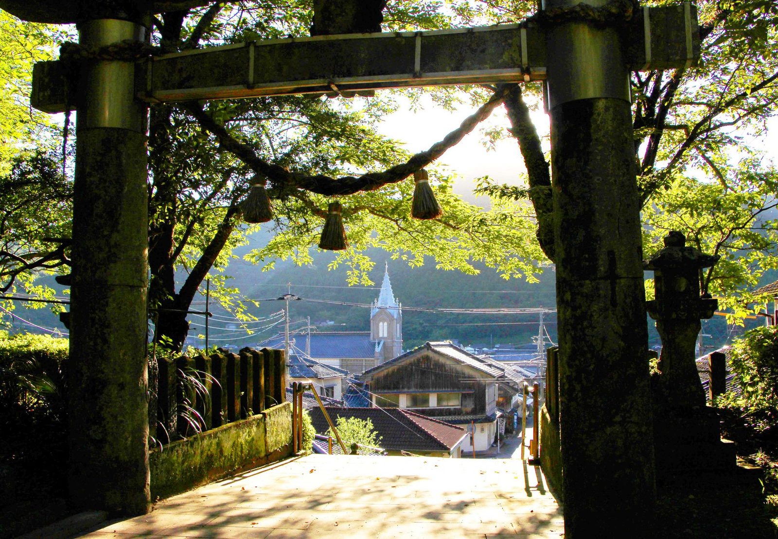 The torii gate at Sakitsu Suwa Shrine framing the village rooftops and the church spire.