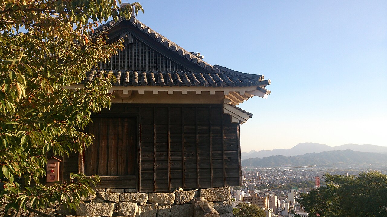 A wooden turret of Matsuyama Castle on its hilltop, with the city and mountains below