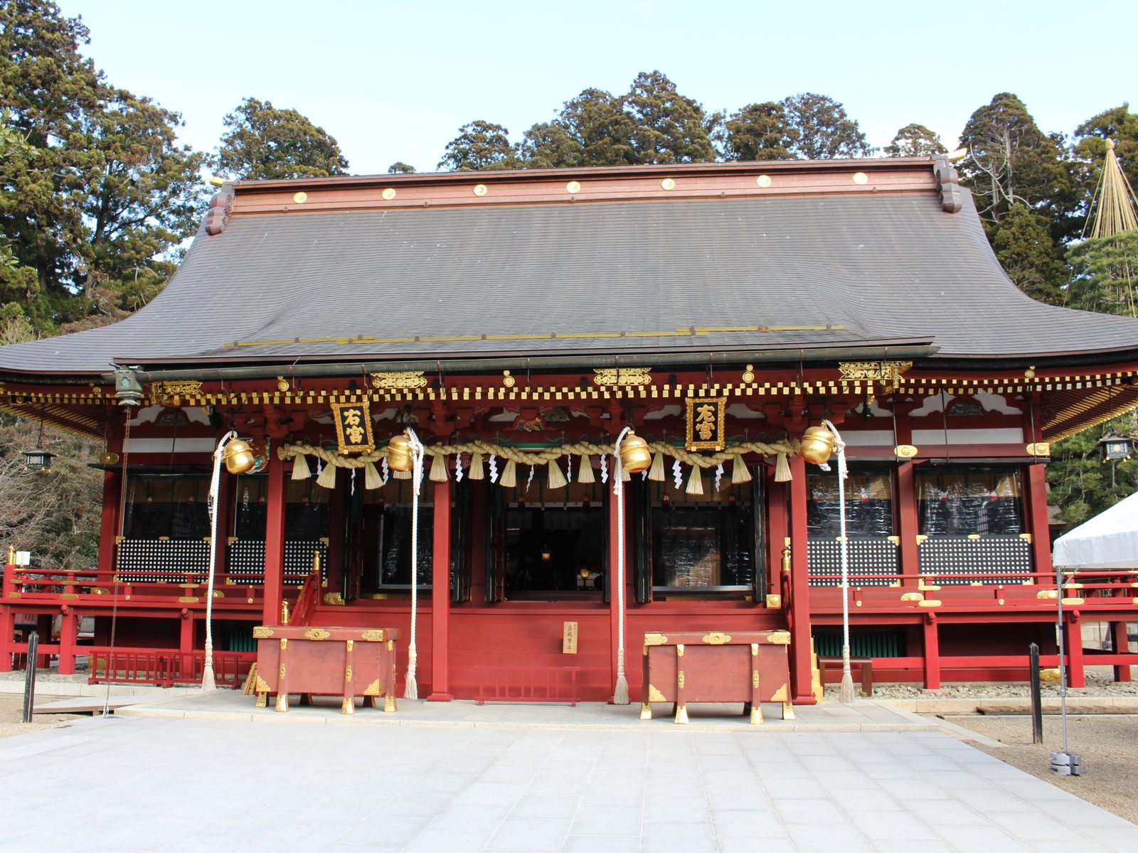The red-and-gold main hall of Shiogama Shrine seen across an open paved courtyard under a clear sky