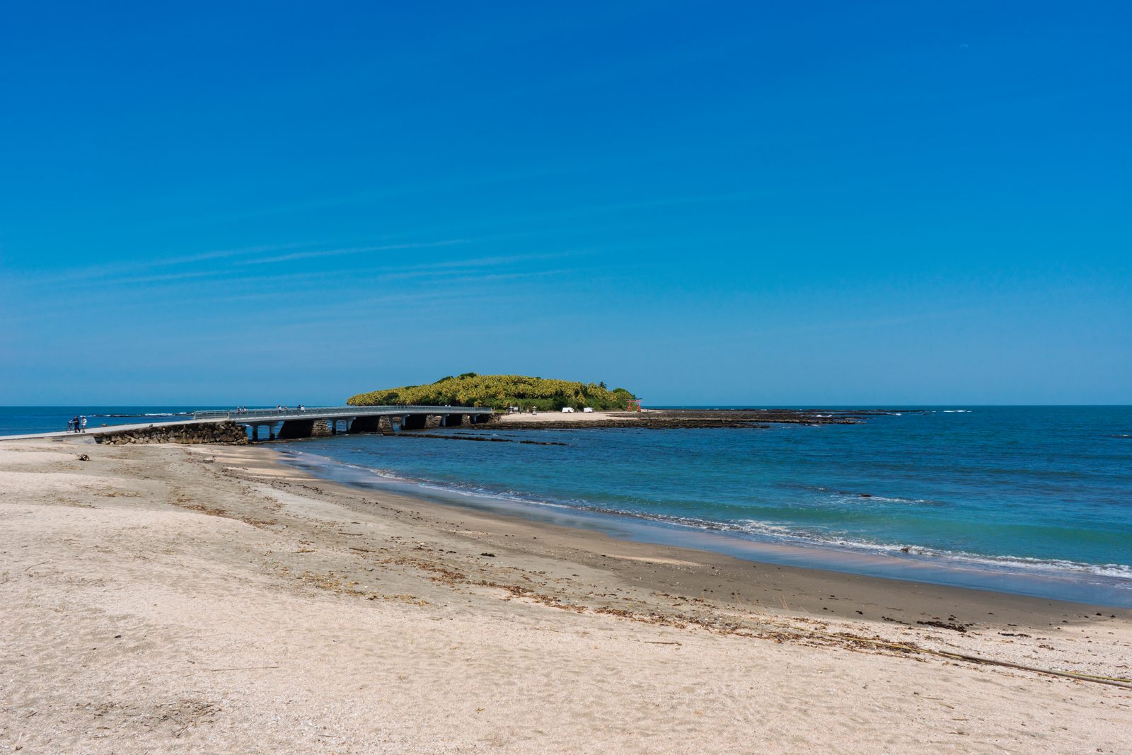 Aoshima island seen from a sandy beach, with the low bridge leading out to it