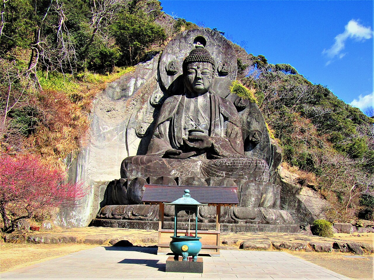 The Nihon-ji Daibutsu, a large stone Buddha carved into the cliff face of Mount Nokogiri, with plum blossoms below.