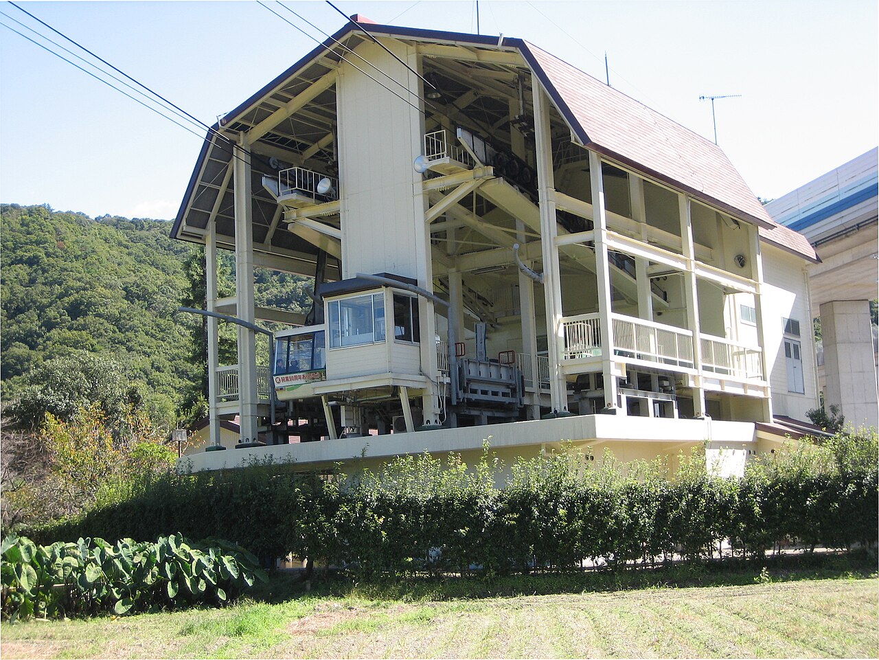 The lower station of the Mount Shosha Ropeway, a pale timber-framed shed with a cabin waiting under the wooded hillside.