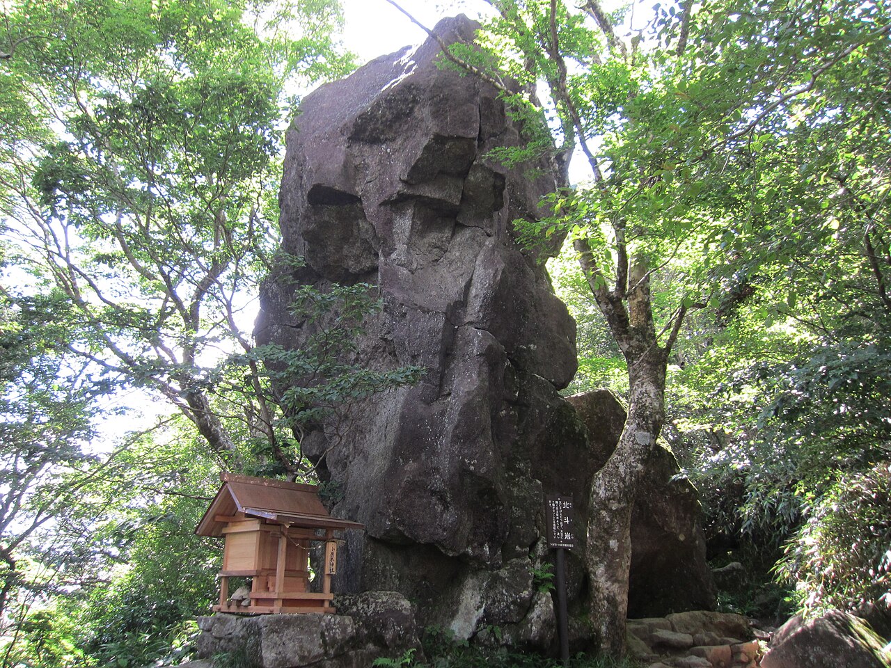 Hokuto-iwa, a tall boulder standing beside a small wooden shrine among trees on the slope of Mount Tsukuba.