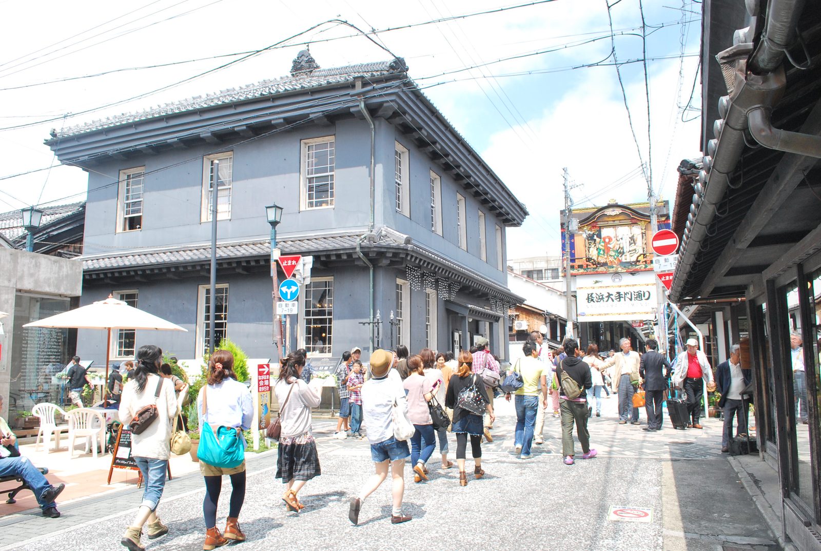 A street in Kurokabe Square lined with grey two-storey Western-style buildings, people walking, and the gate of Otemon-dori with a festival-float signboard beyond