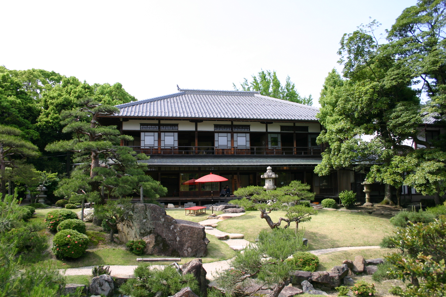 The two-storey wooden building of Keiunkan, with pines, stone lanterns in the garden and a red parasol on the veranda