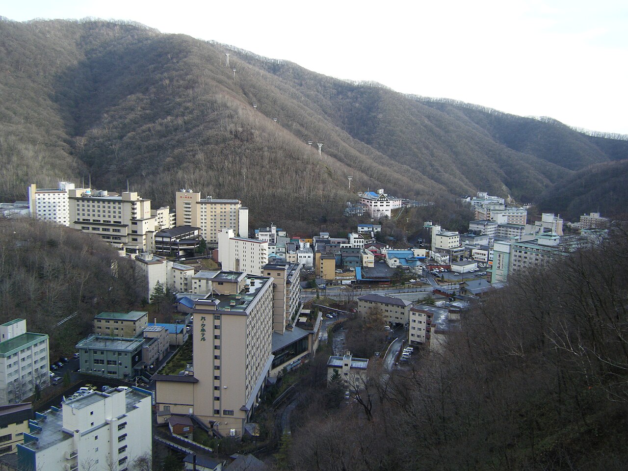 Noboribetsu Onsen seen from above: hotel blocks packed into a narrow wooded valley, with forested ridges rising on every side.