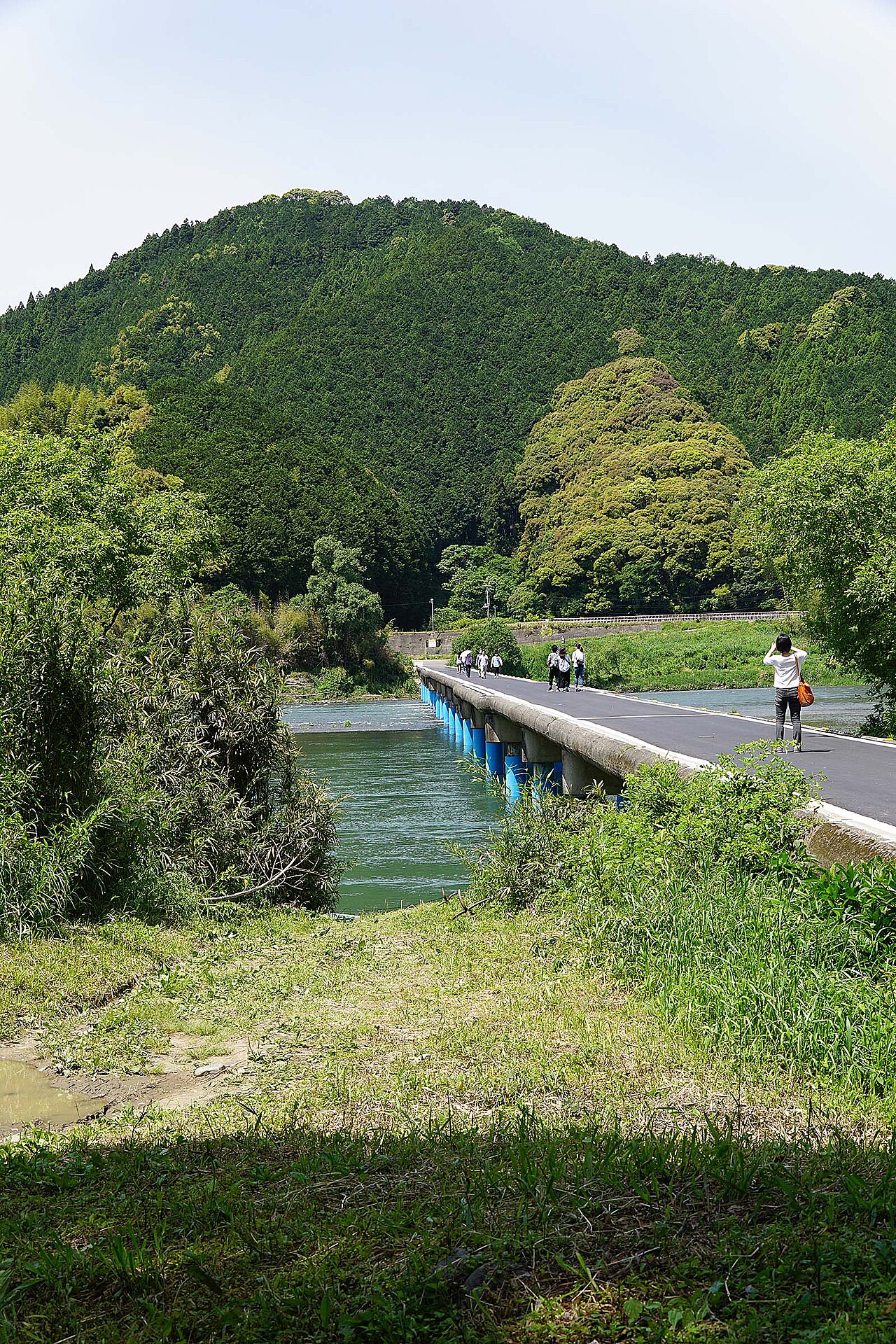 A low sunken bridge on blue piers crossing the green water of the Shimanto River