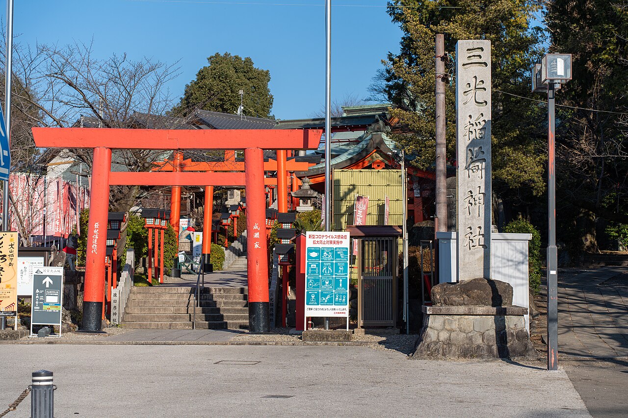 A row of bright red torii gates climbing a stone staircase to Sanko Inari Shrine, beside a stone marker pillar carved with the shrine's name.