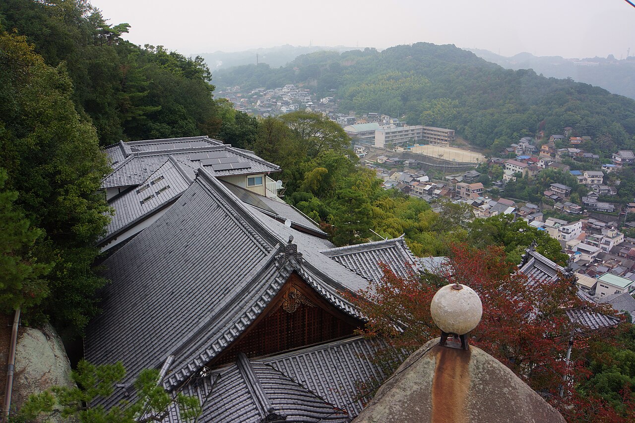 The tiled roofs of Senkoji temple on the hillside, with the town of Onomichi and the water beyond seen through the pines.