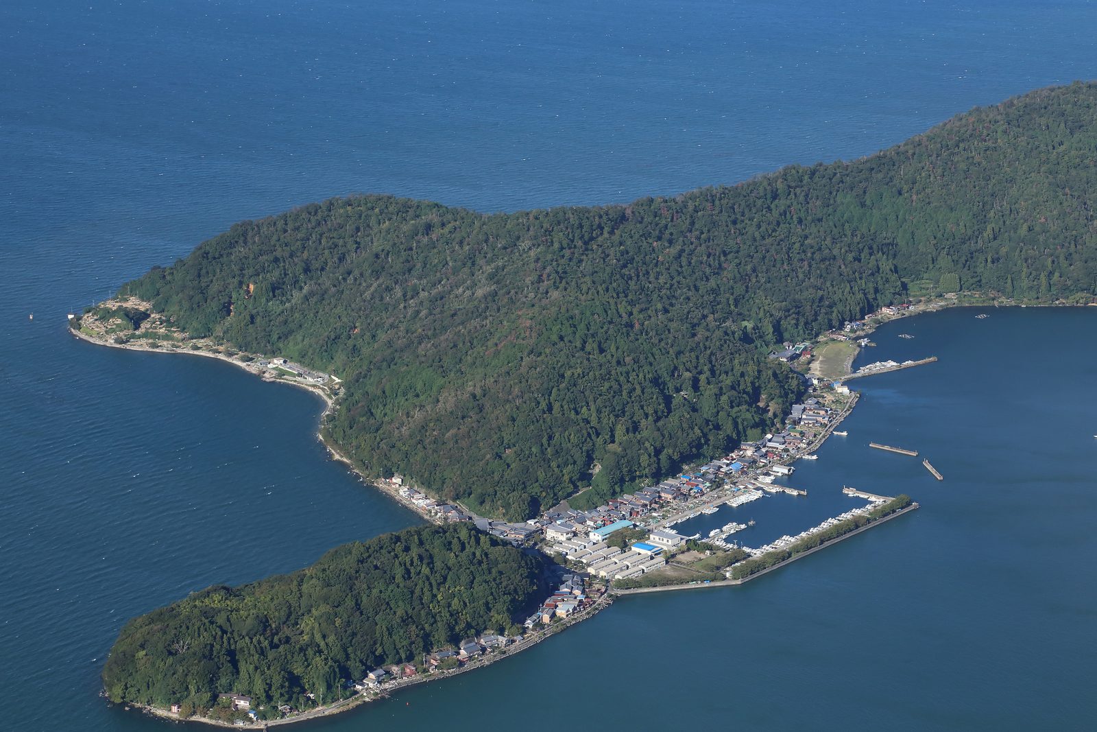 Aerial view of Okishima in Lake Biwa, with the fishing village and its harbor packed along the narrow shore below the wooded hills.