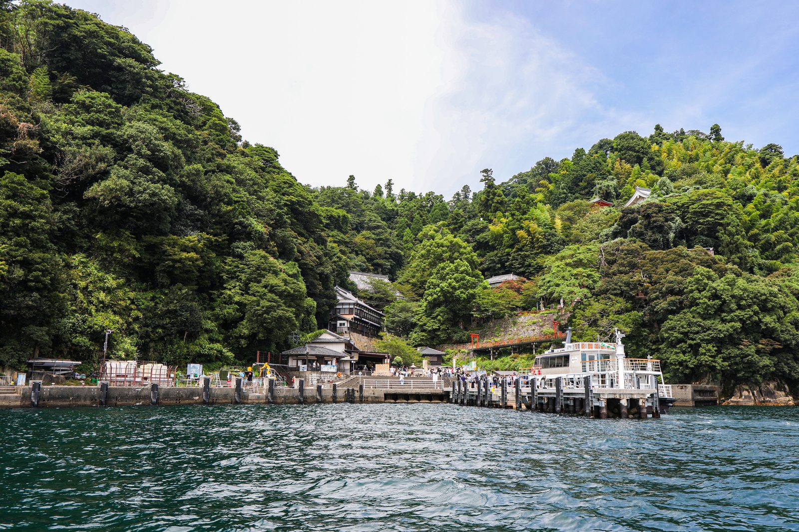 Tourist boat moored at the pier on Chikubushima, with wooded green slopes and temple buildings rising behind the landing