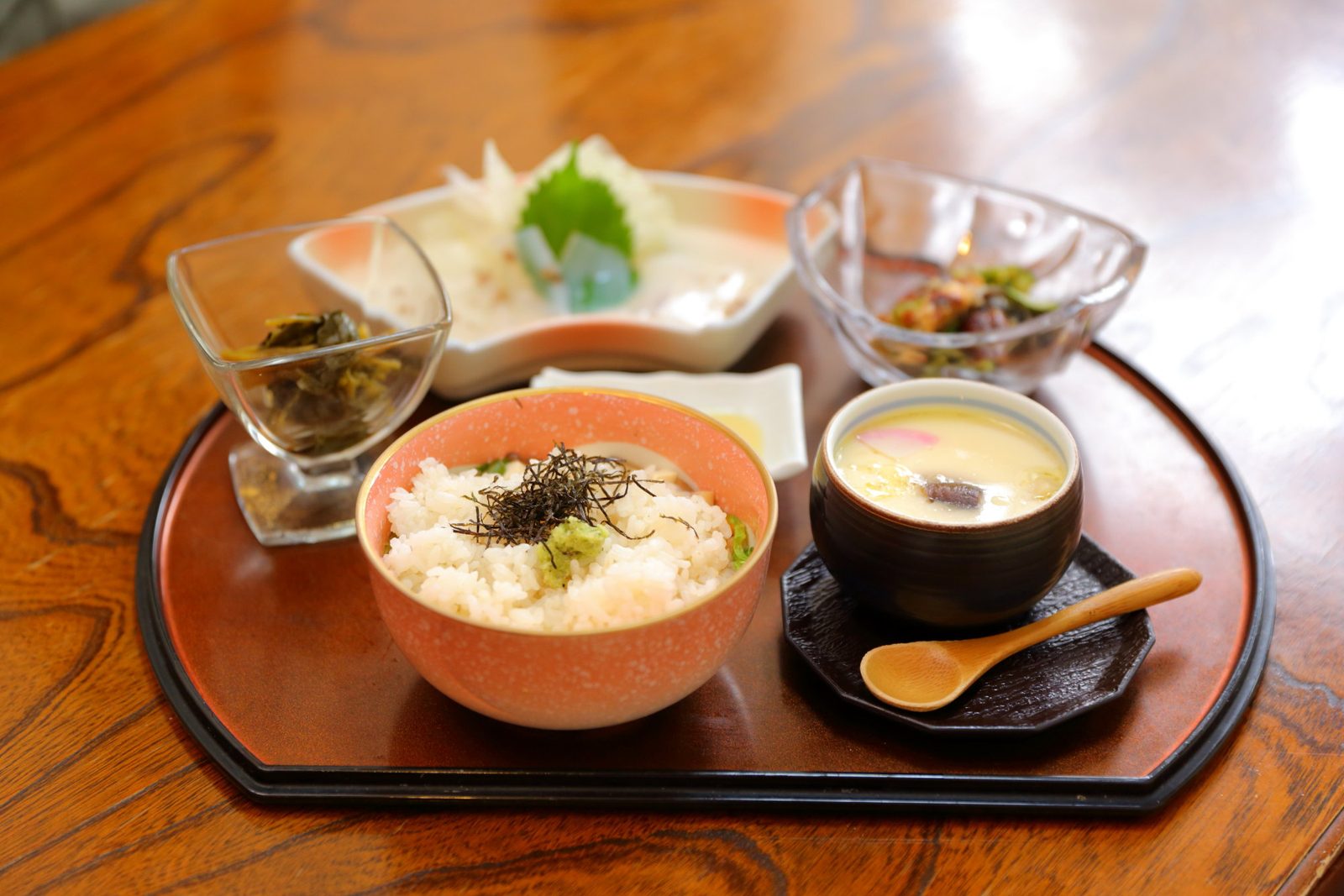 A Tsuwano uzume-meshi set on a lacquer tray: rice topped with shredded nori and wasabi, a cup of savoury egg custard with a wooden spoon, pickles and small side dishes.