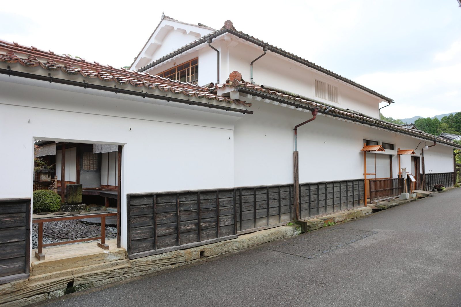 A long white-plastered storehouse-style house with a red-tiled roof and dark lower walls on a quiet street in Omori