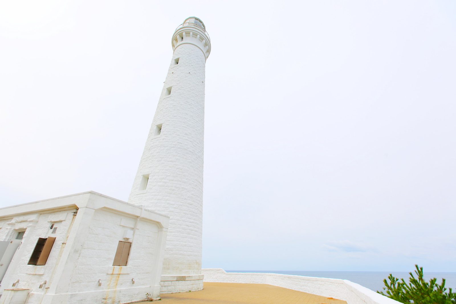 The white stone tower of the Izumo Hinomisaki Lighthouse against a pale sky, with the sea beyond the wall