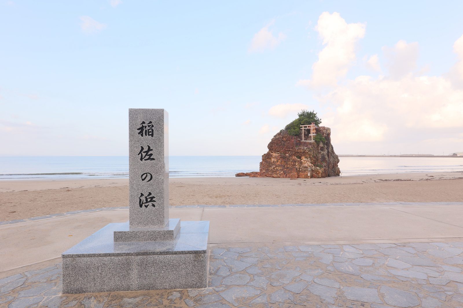 The stone marker at Inasa beach, carved with the beach's name, with a rock islet just offshore