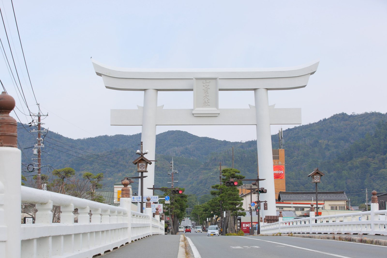 The tall white great torii that spans the road and its bridge, with the name of Izumo Taisha on its plaque