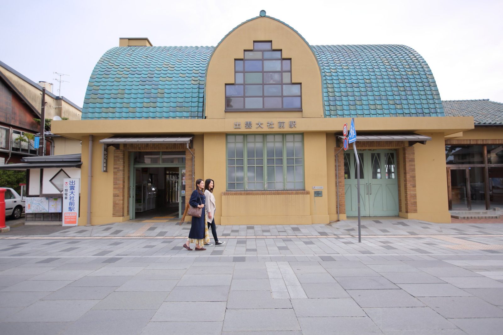 The Art Deco building of Izumo Taisha-mae Station, with a rounded roof of green tiles and yellow walls