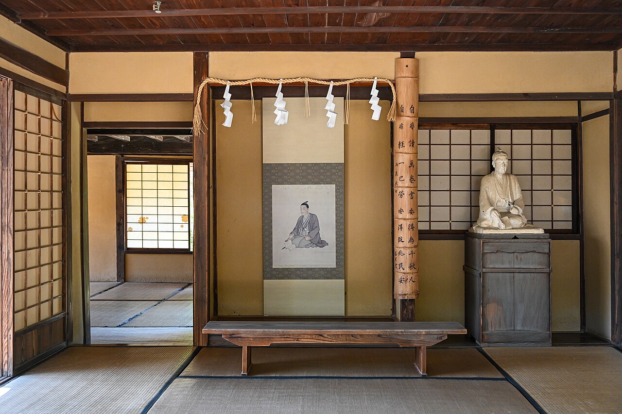 The tatami classroom inside Shokasonjuku at Shoin Shrine in Hagi, with a hanging scroll portrait of Yoshida Shoin, a low wooden desk and paper screens
